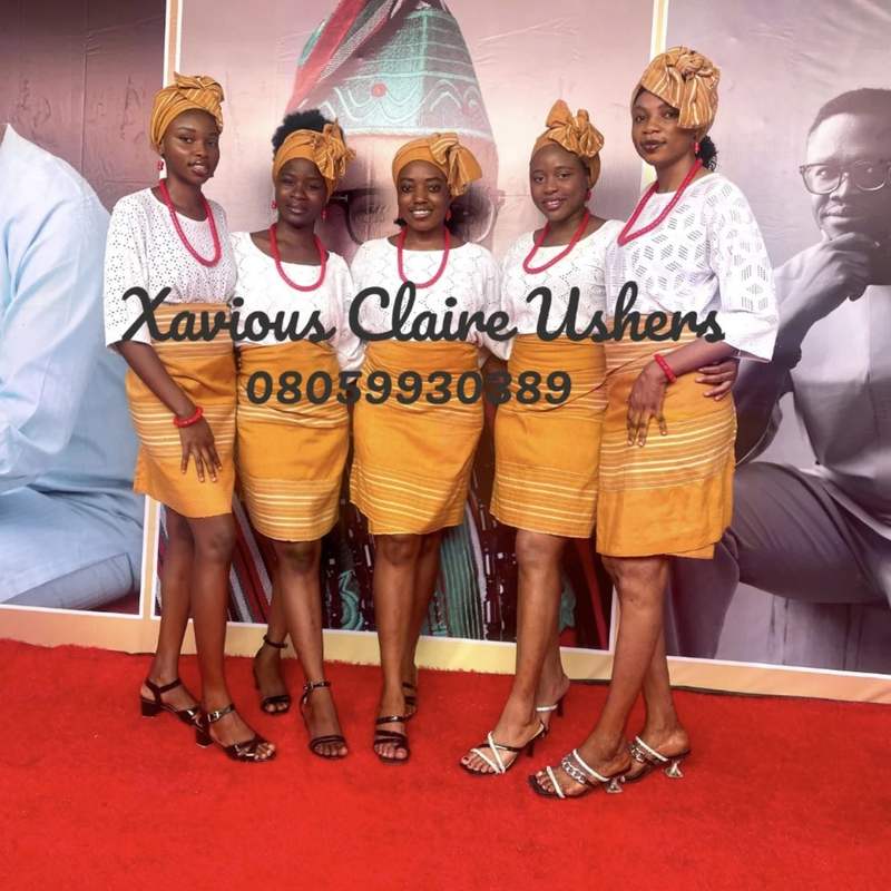 Five Xavious Claire hostesses in matching orange and white lace, posed on a red carpet at a traditional wedding
