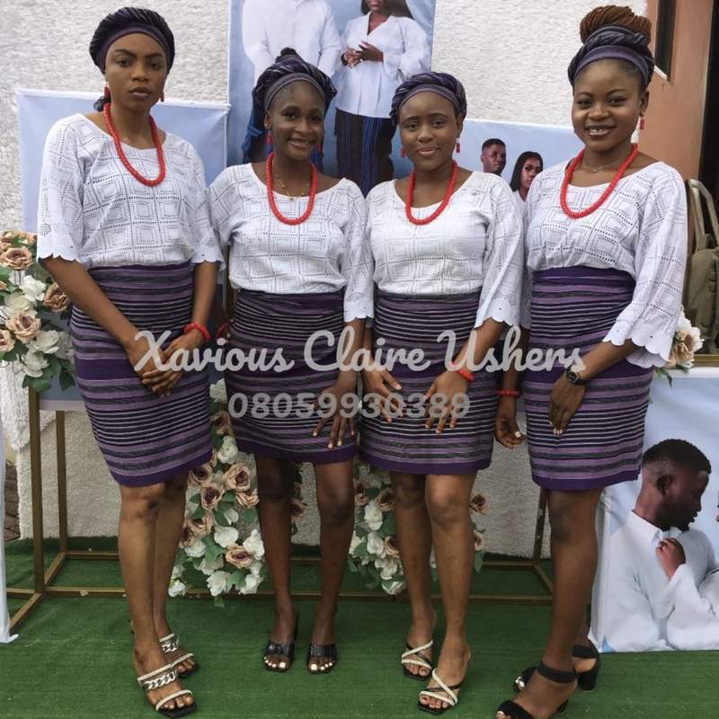 Four Xavious Claire hostesses in white lace and purple wrappers beside a floral backdrop