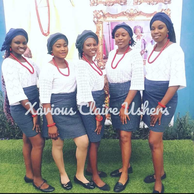 Five Xavious Claire hostesses in white lace, navy wrappers and coral beads at a traditional ceremony