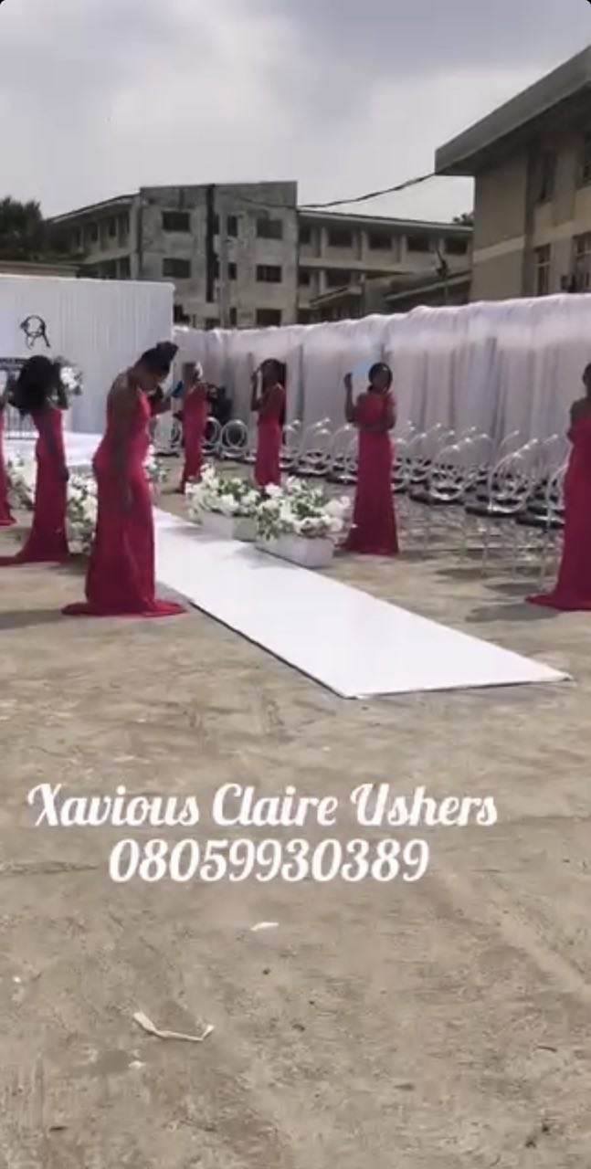 Xavious Claire hostesses in burgundy gowns lined either side of a white aisle runner before an outdoor ceremony